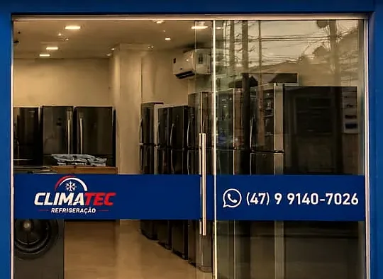Detalhe da vitrine da loja, com eletrodomésticos expostos atrás do vidro e o telefone no letreiro da porta